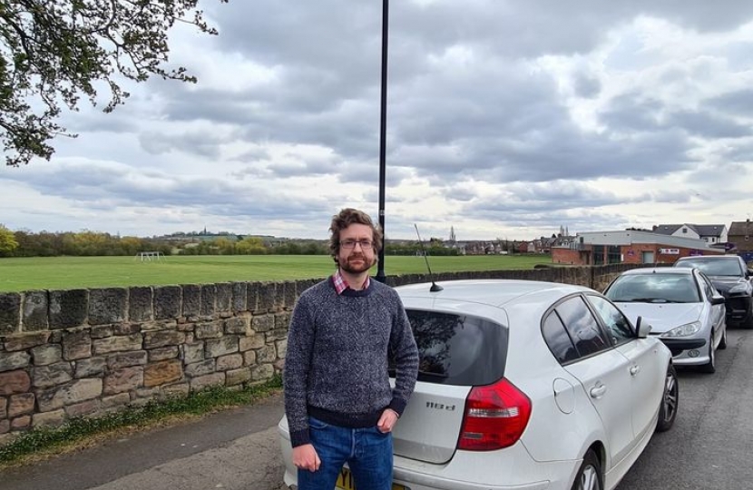 Alexander Stafford stands near parked vehicles on road